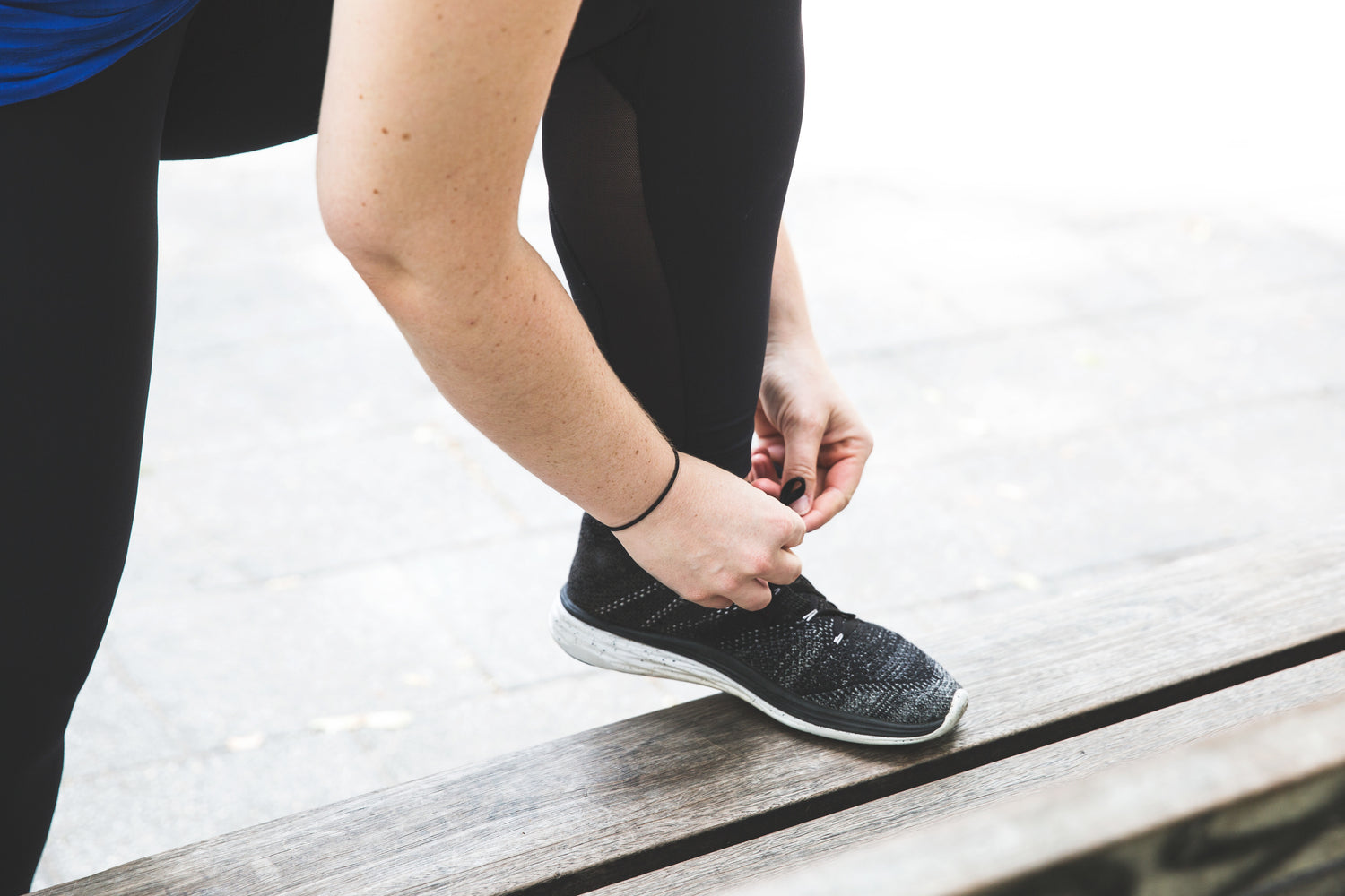 une personne noue ses lacets avec le pied sur un banc