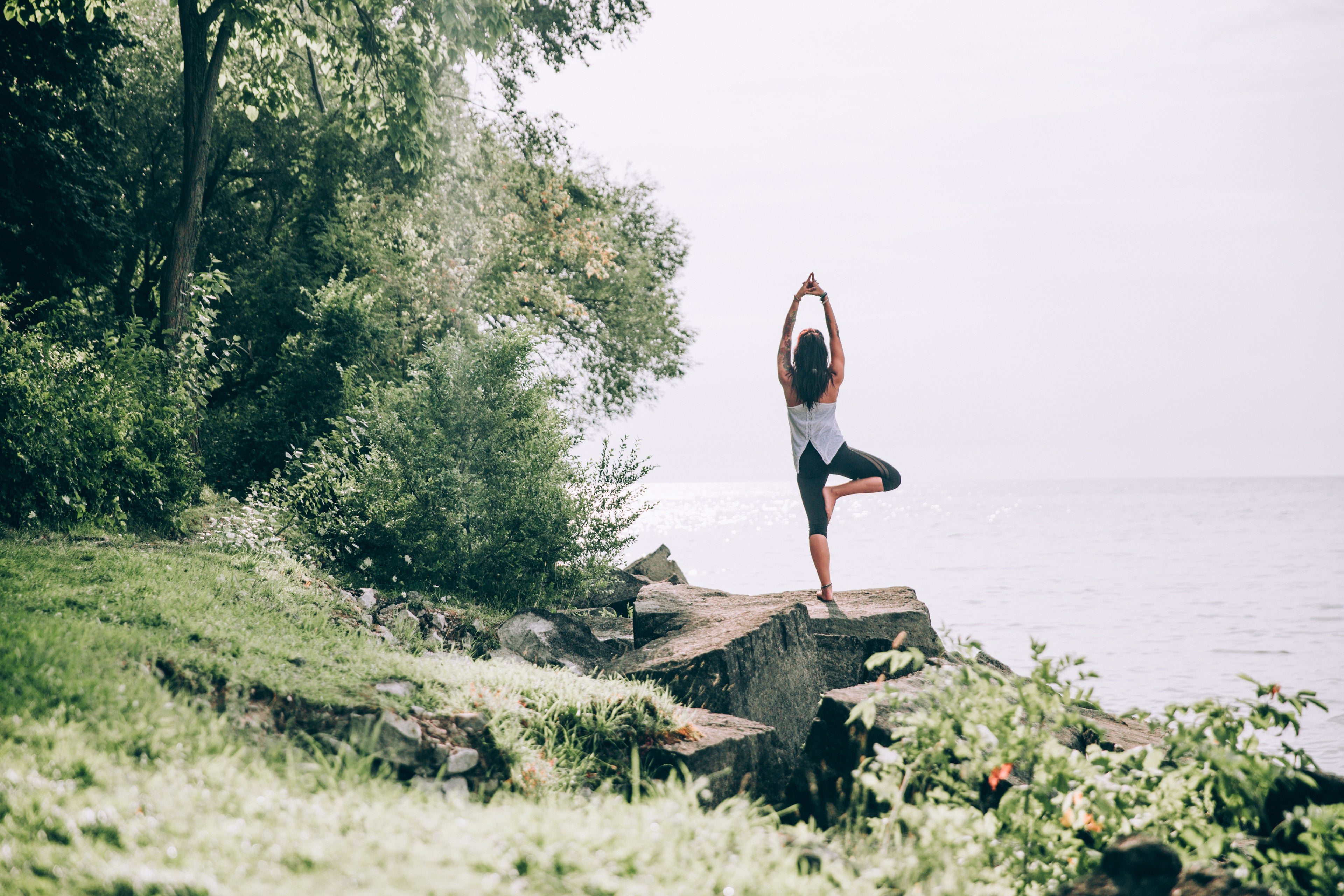 femme qui fait une pose de yoga sur un rocher face à la mer au milieu de la nature