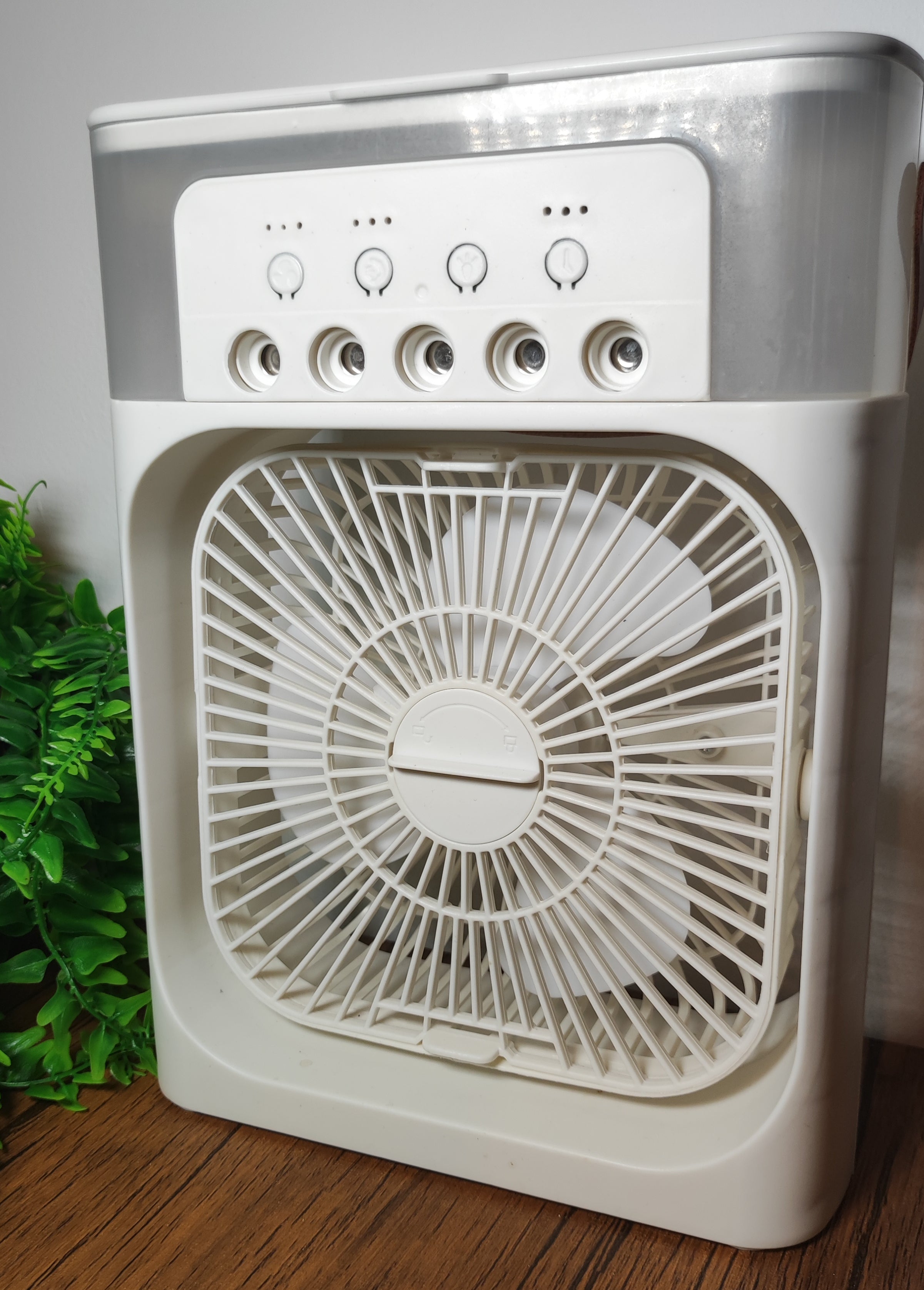 ventilateur humidificateur pose sur une table avec un mur blanc et des feuilles